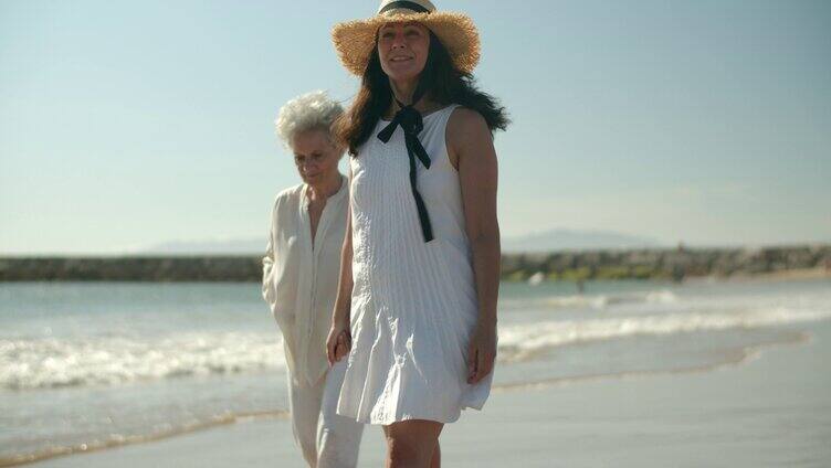 年轻女人陪同老人在沙滩上踩着海浪散心