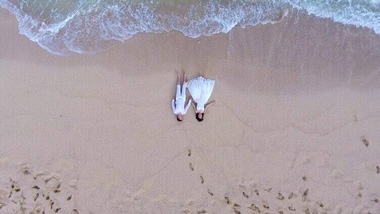 俯拍浪漫情侣躺在沙滩上牵手海浪来袭