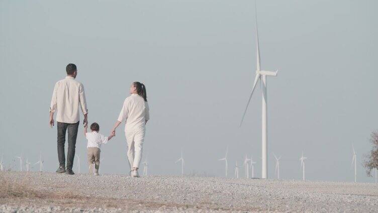后视图，一家三口，两岁的小男孩在风力涡轮机之间自由行走。教育孩子可持续发展的概念。