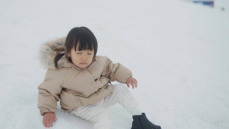 女婴穿着暖暖的冬衣坐在雪地上动来动去