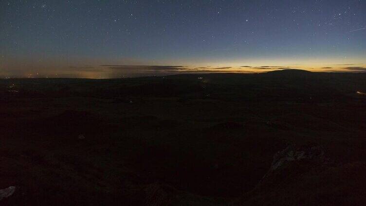 在英国威尔士的布雷肯国家公园的黑山，白天到晚上的时间在丘陵景观上流逝，美丽的日落和云朵在星星前移动