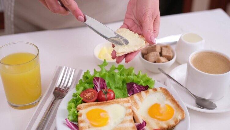 一名女子将黄油涂在烤面包上，餐桌上方是美味的蛋洞吐司早餐