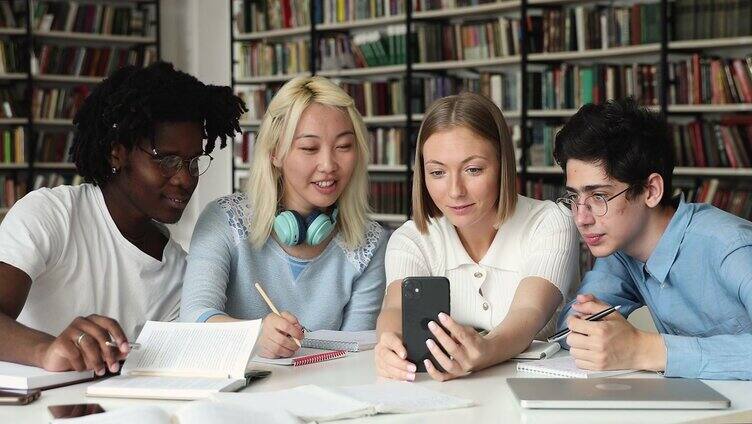 不同的学生小组坐在图书馆玩手机