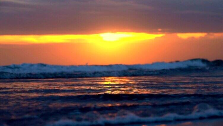 近距离观察:在巴厘岛戏剧性的粉红色日落时，海浪冲刷着沙滩