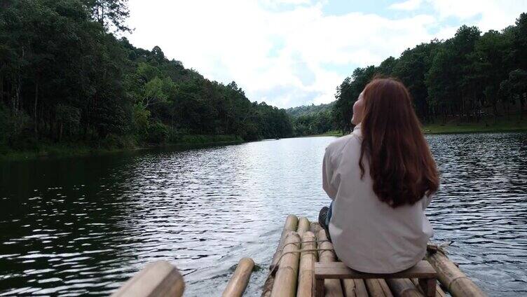 后视图的女性旅行者坐在和骑竹筏在湖中