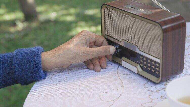 老妇人在后院用手转动老式收音机的旋钮。