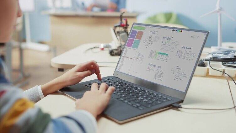 小学计算机科学课堂:一个孩子使用笔记本电脑设计和编程机器人课堂的肩膀视图