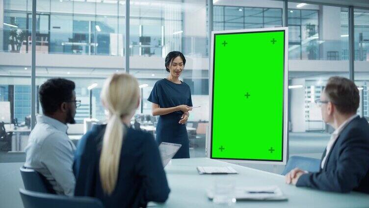 女运营经理为一组经济学家做会议报告。亚洲妇女使用数字白板与垂直绿色屏幕模拟显示。在商务办公室工作的人。