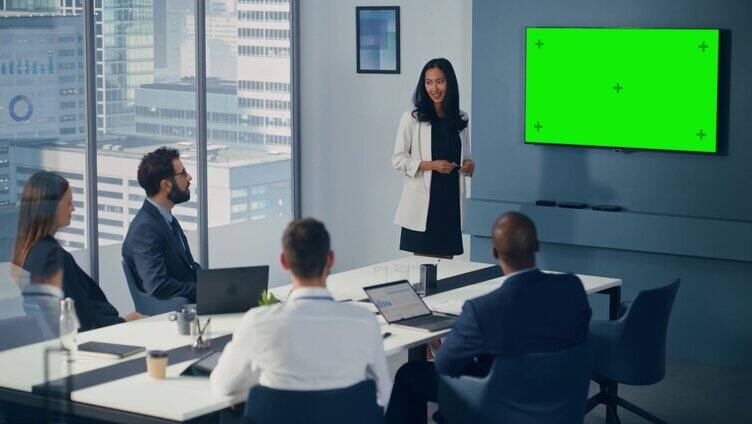 多元办公室会议室会议:亚洲女性项目经理用绿屏色度键墙电视为快乐投资团队呈现数字投资机会。静态的广角镜头