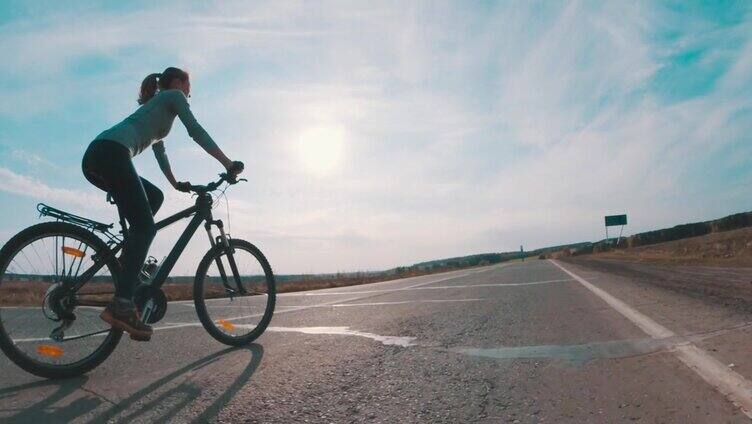 骑自行车的女人。在阳光明媚的日子里，一名年轻女子骑着自行车走在柏油路上