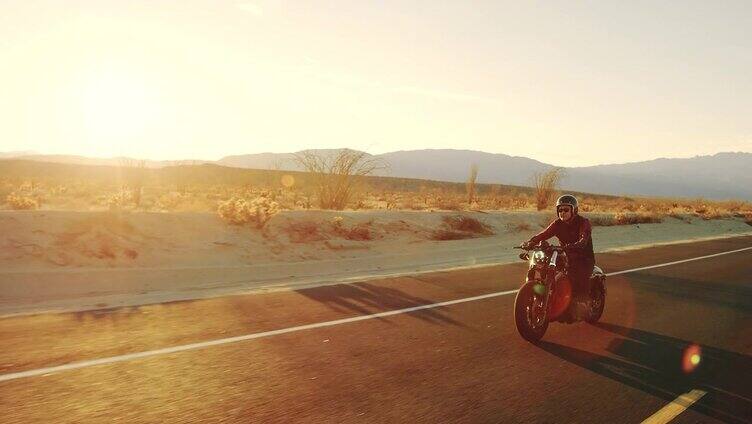 快乐的人骑着老式黑色摩托车在沙漠公路上日落