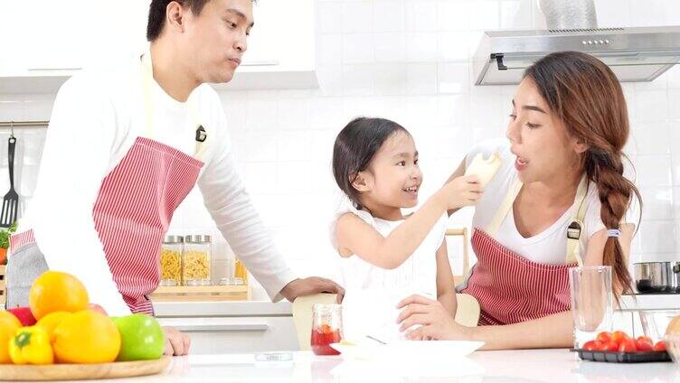 4k慢镜头，年轻的亚洲父亲母亲和女儿快乐和有趣的果酱面包和喂父母在一个现代化的白色厨房。
