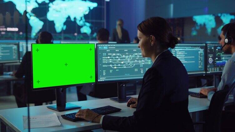 自信的女性数据科学家在大型基础设施控制和监控室用绿屏模拟个人电脑工作。女工程师在办公室里和同事们一起使用电脑。