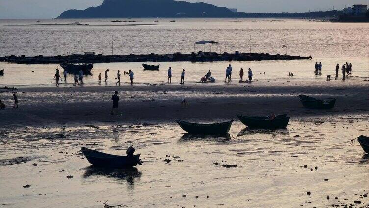 晚霞下，游客们在海滩上赶海游玩