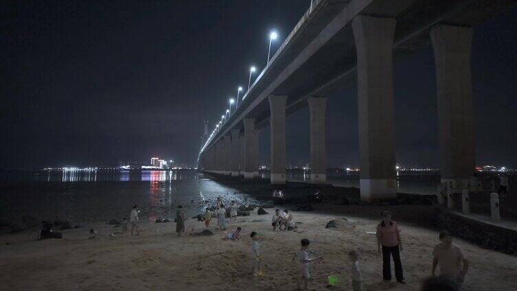 夜晚游客们在湛江海湾大桥下的沙滩游玩