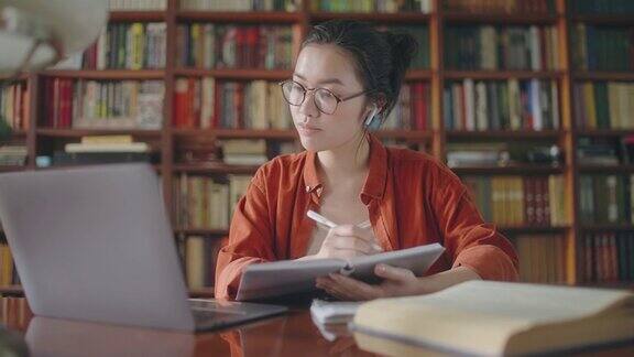 集中的亚洲学生记笔记在图书馆上在线课程