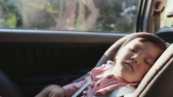 慢动作可爱的亚洲学步女孩坐在汽车座椅和睡觉而与家人旅行