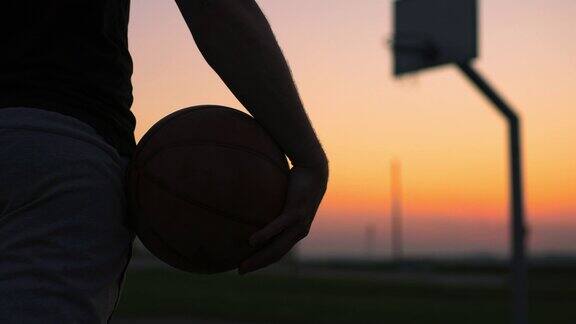 黄昏时分一个年轻人带着篮球走出室外的篮球场