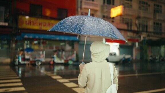 一位年长的妇女在一个雨夜走在夜市上