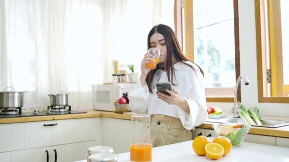 快乐的亚洲女人在厨房喝橙汁健康的饮食和健康