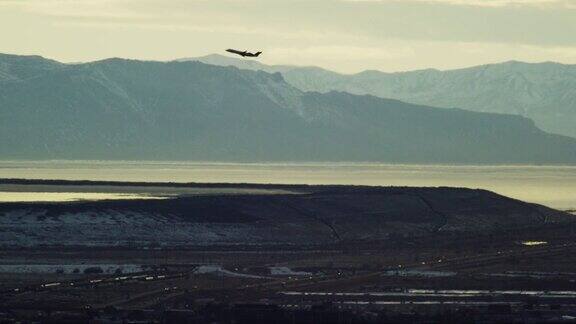 一架商用客机的剪影飞过犹他州的大盐湖和雪山在一个多云的日子在冬天日落