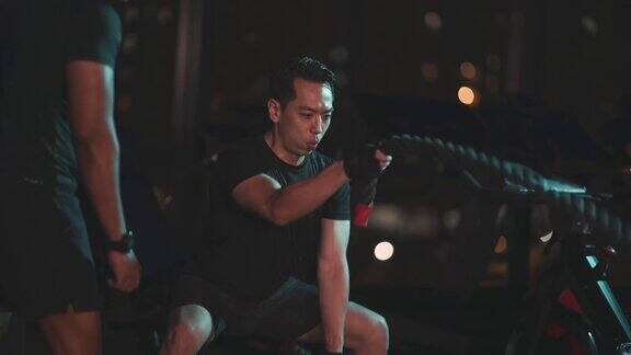 亚洲印度私人教练鼓励亚洲华人中成年人在健身房练习有挑战性的战斗绳