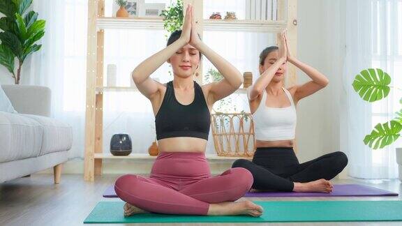 亚洲女性朋友一起在家做瑜伽普拉提迷人的女孩穿着运动服用垫子在家里的客厅里度过自由的休闲时光进行保健运动