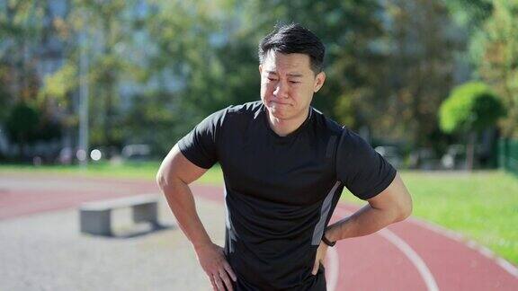 年轻的亚洲运动员在城市体育场遭受背部疼痛运动损伤肌肉痉挛一个穿着运动服的英俊男子腰痛和问题