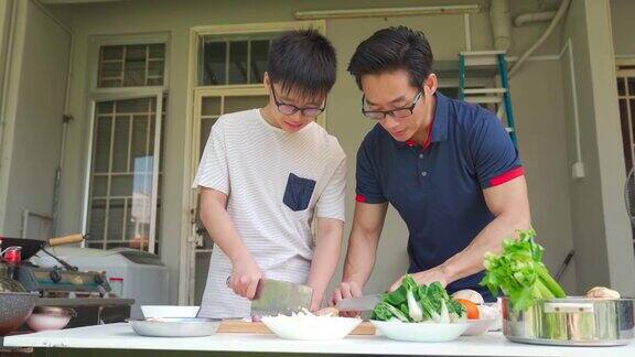 周末的时候亚洲华人父亲和儿子在自家后院的厨房做饭为家人准备晚餐
