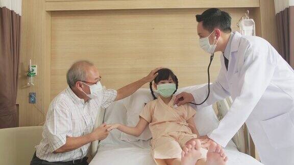 亚洲医生在康复室的床上用听诊器测量小孩的心率冠状病毒大流行期间戴口罩的男女检查女童父亲照顾孩子