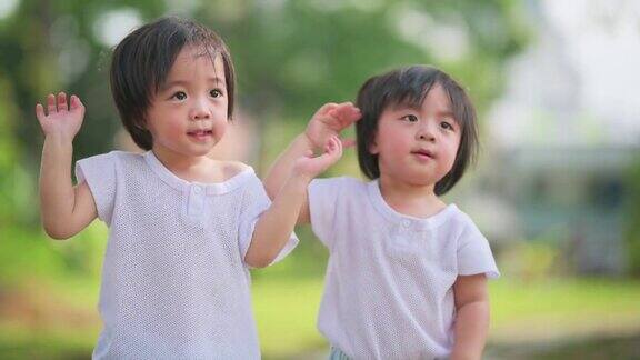 在草坪公园里一对可爱的亚洲华人双胞胎男婴向他们的父母挥手