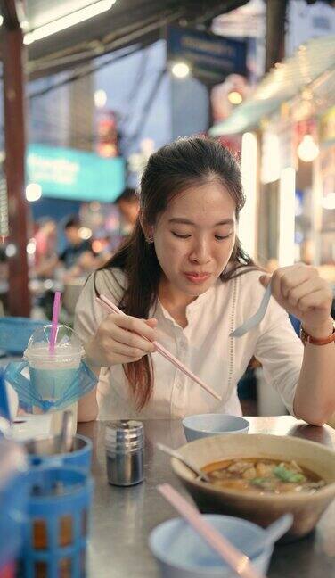 年轻的亚洲游客坐在路边品尝美味的街头小吃在泰国yaowarat