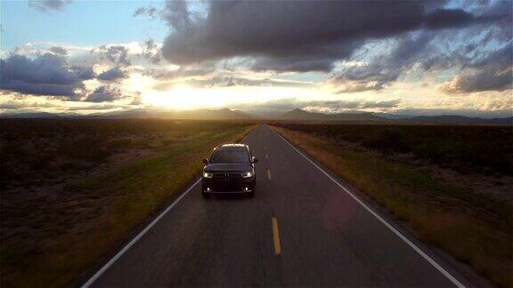 图片:金色的夕阳下一辆黑色SUV行驶在空旷的乡村道路上