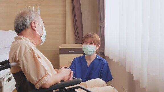 在医院照顾坐在轮椅上的成熟男性病人的亚洲护士年轻妇女和老人戴上外科口罩以预防covid-19大流行女孩对老人微笑