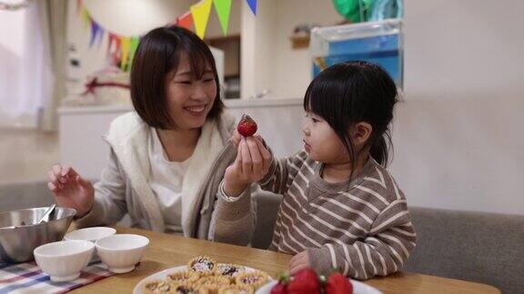 年轻的母亲和女儿在家里把巧克力放在草莓上