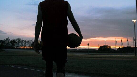 黄昏时分年轻男子走出户外篮球场