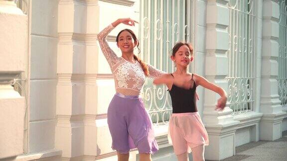 在一个阳光明媚的日子里一名亚洲青少年芭蕾舞演员在一名年轻女芭蕾舞老师的建议下在泰国曼谷当地的街道上练习芭蕾舞活跃的年轻妇女和孩子周末活动和当地地标