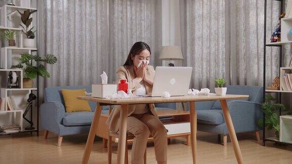 生病的亚洲女商人在家里的客厅用笔记本电脑工作生病的女孩打喷嚏用纸巾擦鼻涕