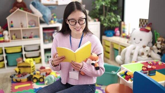 年轻的中国女幼儿教师坐在幼儿园的桌子上读故事书