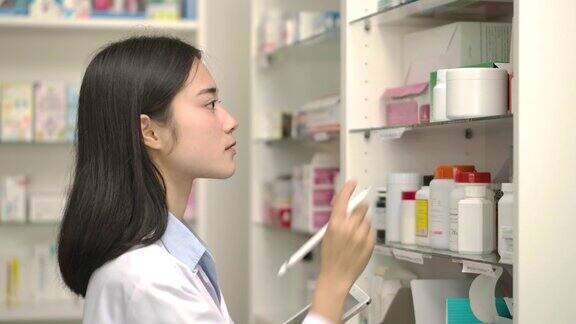 年轻的女药剂师拿着电脑药片使用检查药物细节在药店的盒子