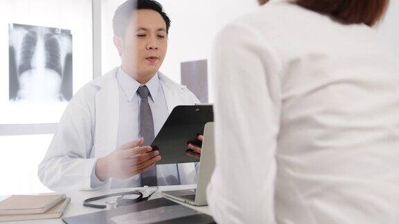 严肃的亚洲男医生正在用剪贴板与女病人坐在医院办公室的桌子前传递好消息谈论结果或症状