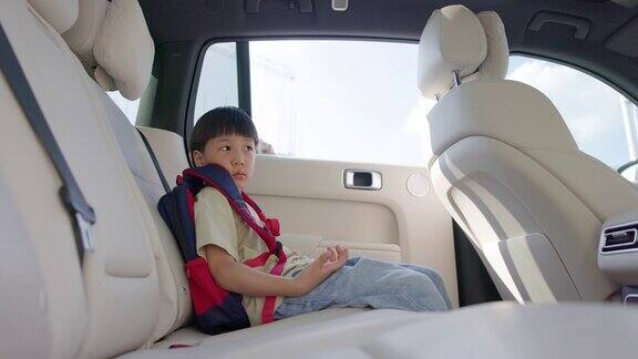 小男孩坐在靠窗的汽车后座上等着他的爸爸