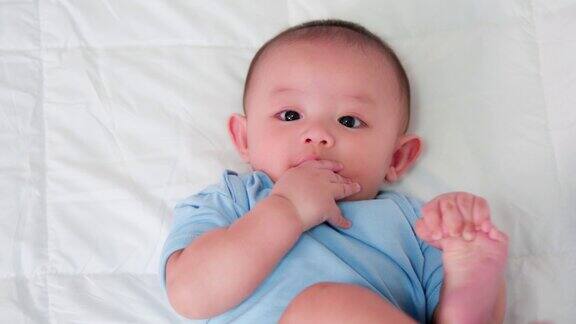 幸福的家庭可爱的亚洲新生宝宝穿着蓝色的衬衫躺在白色的床上玩耍看着镜头笑着笑着幸福的脸天真可爱的小婴儿为人父母和母亲节