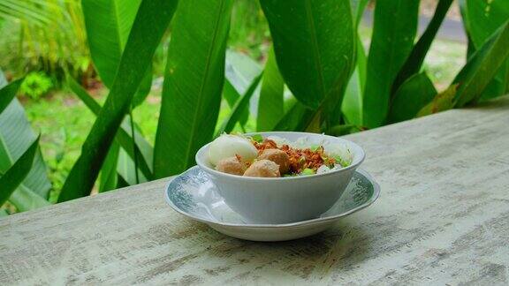 传统的巴厘岛食物盘子与美味的菜肴印尼国家肉丸鸡面条汤或米baksoayam碗服务绿色热带树叶在自然背景