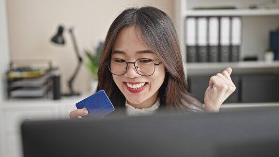 年轻的中国女商务工作者在办公室用电脑和信用卡购物