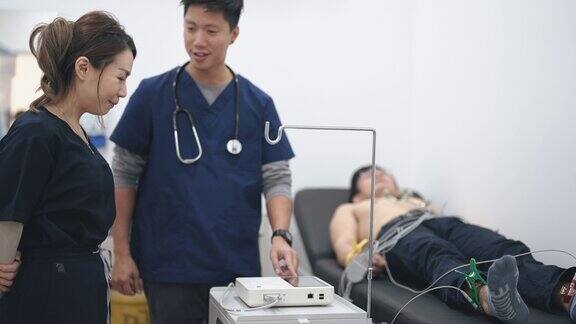 亚洲的中国医生在医院向护士解释给病人做心电图检查