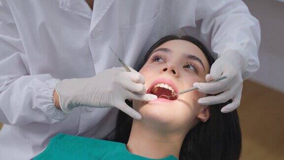 亚洲女牙医在牙科诊所检查年轻女孩病人的牙齿医生使用牙科仪器探查牙齿寻找蛀牙治疗和检查填充问题