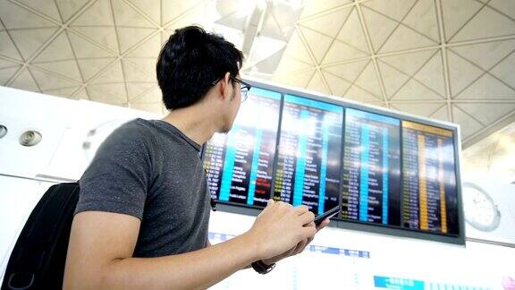 一名亚洲男子在机场盯着登机牌和智能手机