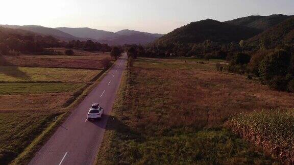 在一个金色的夏日夕阳下一辆白色的汽车行驶在空旷的乡村道路上