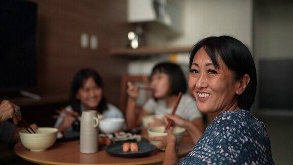 一个快乐的成熟女人和家人在家里吃日本食物的肖像